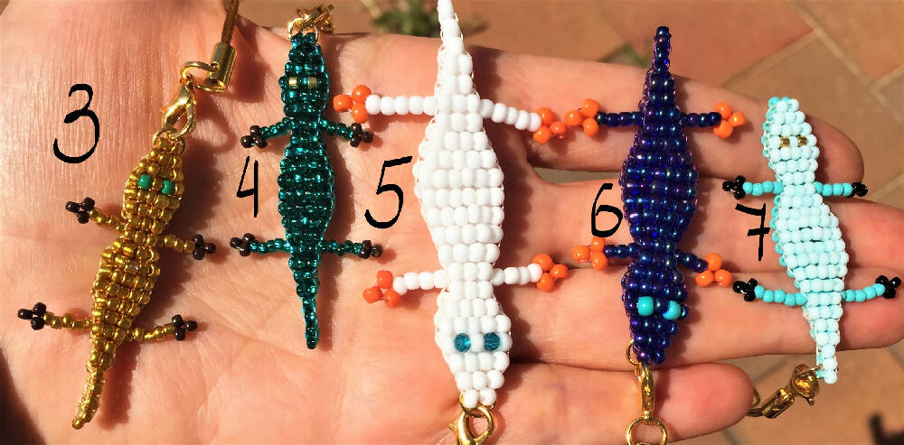 On the palm 5 Naryanabeads beaded crocs.Number 3 next to golden with green eyes, 4 next to emerald with golden eyes, 5 next to large white with blue crystal eyes, number 6 next to shiny dark blue with blue eyes,number 7 next to double colour blue/matte pale blue one